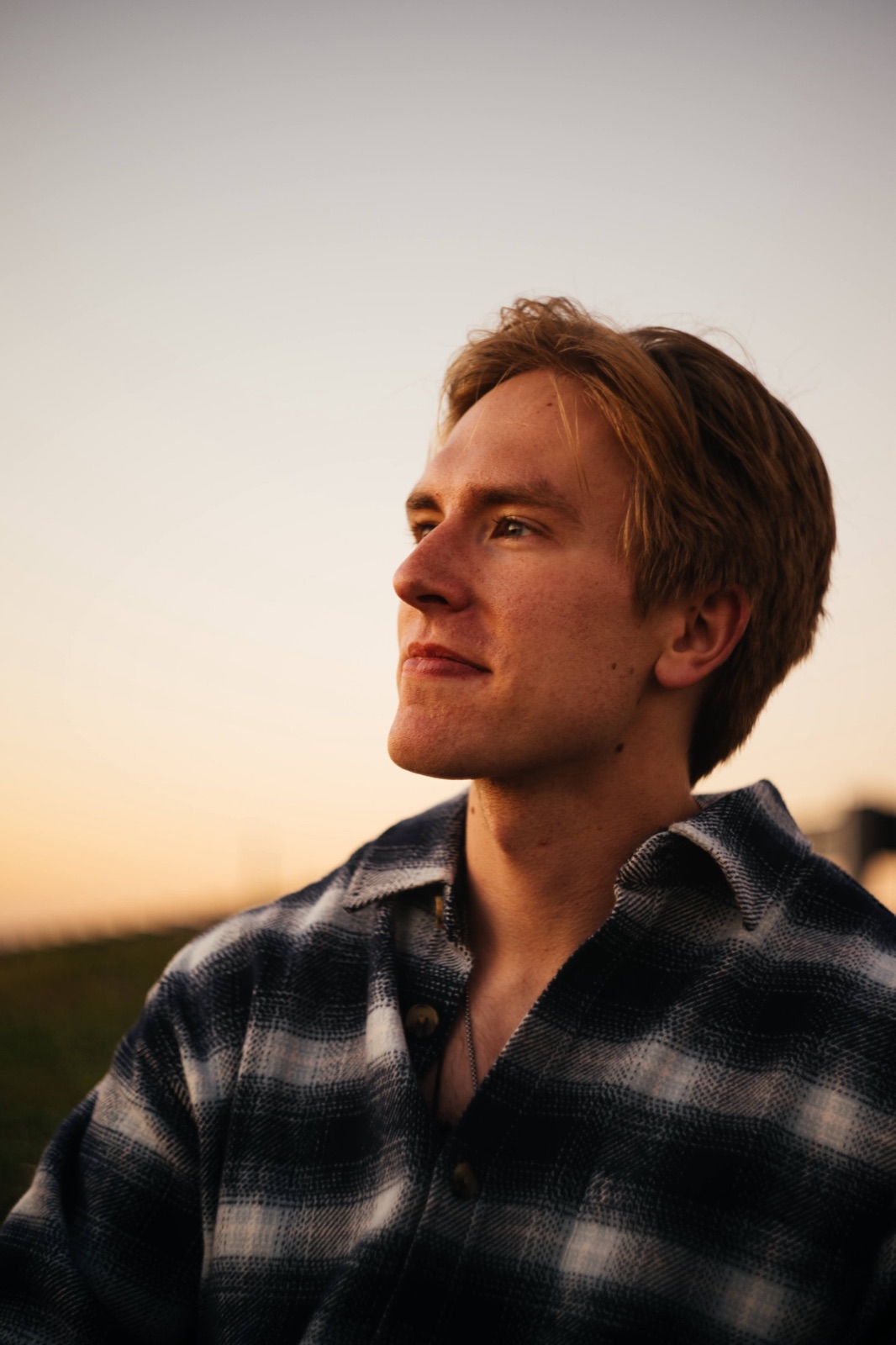Nick looking off into a sunset, wearing a flannel shirt