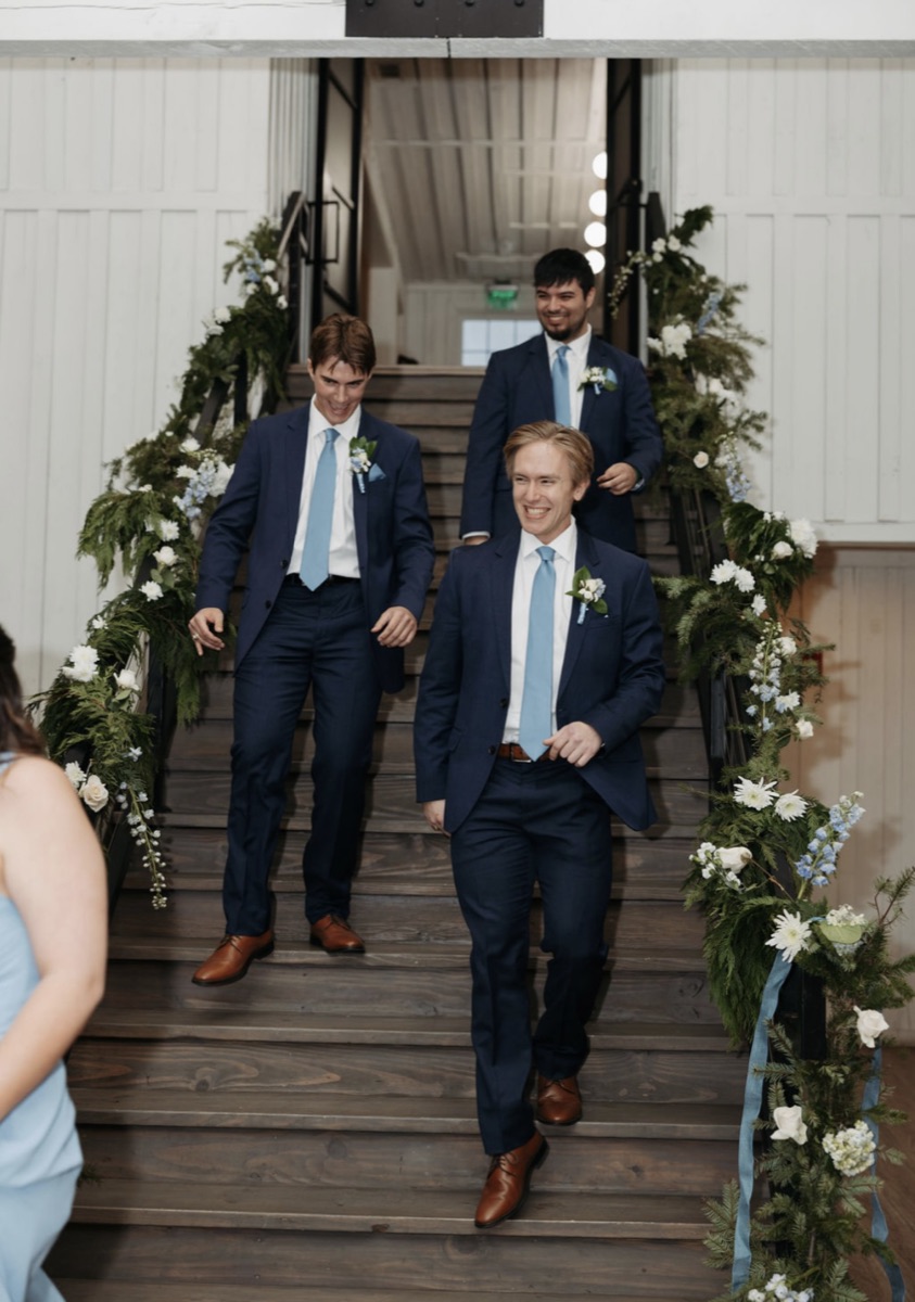 Groomsmen, including Nick, walking down a staircase at a wedding