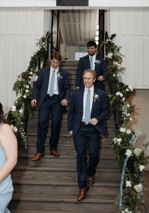 Groomsmen, including Nick, walking down a staircase at a wedding